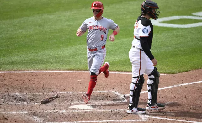 Cincinnati Reds' Matt McLain (9) comes in to score on a double by Austin Hays during the fifth inning of a baseball game past Baltimore Orioles catcher Adley Rutschman, right, Sunday, April 20, 2025, in Baltimore. (AP Photo/Nick Wass)