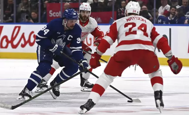 Toronto Maple Leafs' Auston Matthews (34) moves the puck between Detroit Red Wings' Austin Watson (24) and Tyler Motte (14) during the second period of an NHL hockey game Thursday, April 17, 2025, in Toronto. (Jon Blacker/The Canadian Press via AP)