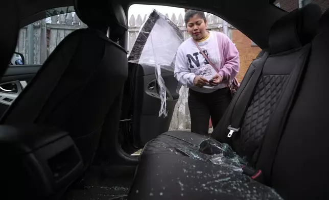 Marilu Domingo Ortiz, whose husband was taken into custody by ICE agents after they smashed a window of their family car, looks at broken glass and damage to their vehicle at their home, Wednesday, April 16, 2025, in New Bedford, Mass. (AP Photo/Charles Krupa)