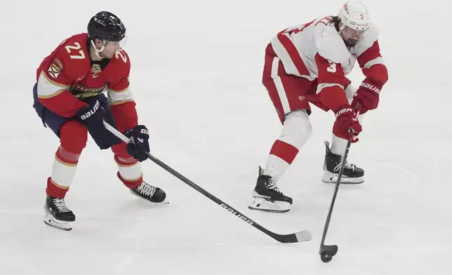 Detroit Red Wings defenseman Justin Holl (3) and Florida Panthers center Eetu Luostarinen (27) go after the puck during the second period of an NHL hockey game, Thursday, April 10, 2025, in Sunrise, Fla. (AP Photo/Marta Lavandier)