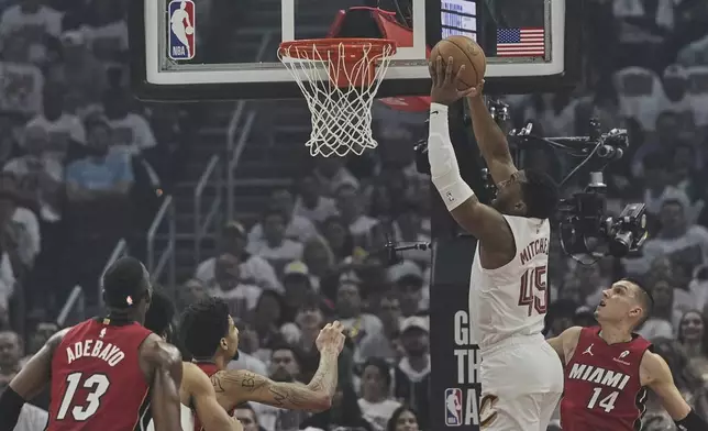 Cleveland Cavaliers guard Donovan Mitchell (45) goes up for a dunk between Miami Heat center Bam Adebayo (13) and guard Tyler Herro (14) in the first half in Game 1 of an NBA first-round playoff series, Sunday, April 20, 2025, in Cleveland. (AP Photo/Sue Ogrocki)