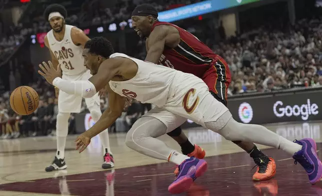 Cleveland Cavaliers guard Donovan Mitchell, front, and Miami Heat center Bam Adebayo, right, reach for the ball in the first half in Game 1 of an NBA first-round playoff series, Sunday, April 20, 2025, in Cleveland. (AP Photo/Sue Ogrocki)