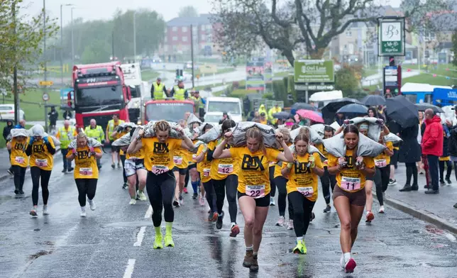 Women's race competitors including eventual winner Ferne Gardener, no. 11, right, run with a 20kg sack of coal over a 1.1 km course during the World Coal Carrying Championships in Ossett, West Yorkshire, England, Monday, April 21, 2025. (AP Photo/Jon Super)