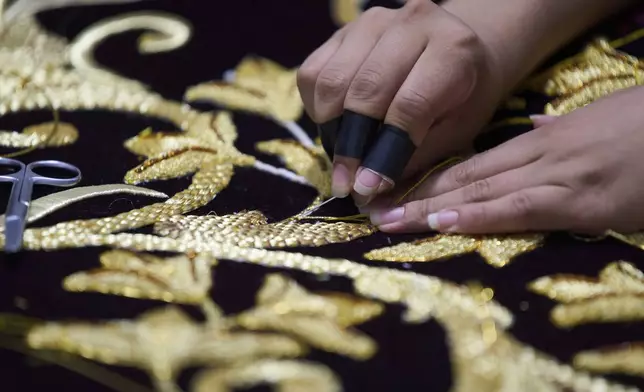 A weaver applies gold-colored pieces to the tunic for a statue of the Virgin Mary at the Maria Auxiliadora embroidery workshop in San Miguel Escobar, Guatemala, Wednesday, April 2, 2025. (AP Photo/Moises Castillo)