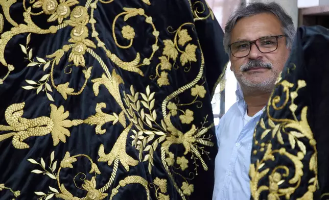 Guatemalan artist Alejandro Juarez poses with his finished tunic to be worn by a statue of the Virgin Mary, at the Maria Auxiliadora embroidery workshop in San Miguel Escobar, Guatemala, Wednesday, April 2, 2025. (AP Photo/Moises Castillo)