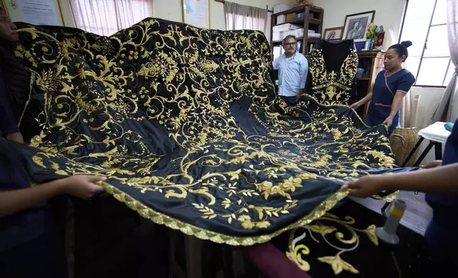 Guatemalan artist Alejandro Juarez, top center, and weavers display their finished tunic to be worn by a statue of the Virgin Mary, at the Maria Auxiliadora embroidery workshop in San Miguel Escobar, Guatemala, Wednesday, April 2, 2025. (AP Photo/Moises Castillo)