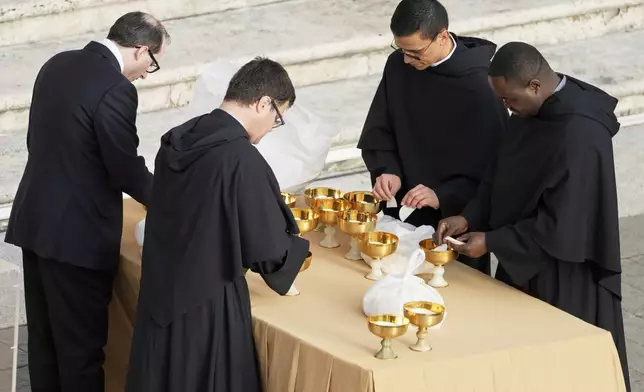 Priests and an assistant make arrangements ahead of the funeral of Pope Francis in St. Peter's Square at the Vatican, Saturday, April 26, 2025. (AP Photo/Markus Schreiber)