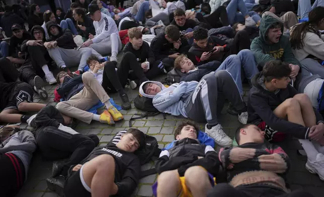 Faithful rest on the ground as they wait for the funeral of Pope Francis to begin, in St. Peter's Square at the Vatican, Saturday, April 26, 2025. (AP Photo/Emilio Morenatti)