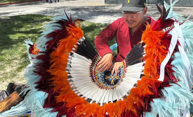 Christian Rangel, who is Navajo and Cherokee and from Tulsa, Oklahoma, talks about the work that went into making his bustle following the grand entry procession during the annual Gathering of Nations powwow in Albuquerque, New Mexico, Friday, May 25, 2025. (AP Photo/Susan Montoya Bryan)