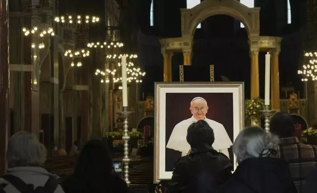 Mourners say prayers and light candles in front of a portrait of Pope Francis inside Westminster Cathedral, in London, Monday, April 21, 2025, following the announcement by the Vatican of the death of Pope Francis. (AP Photo/Alastair Grant)