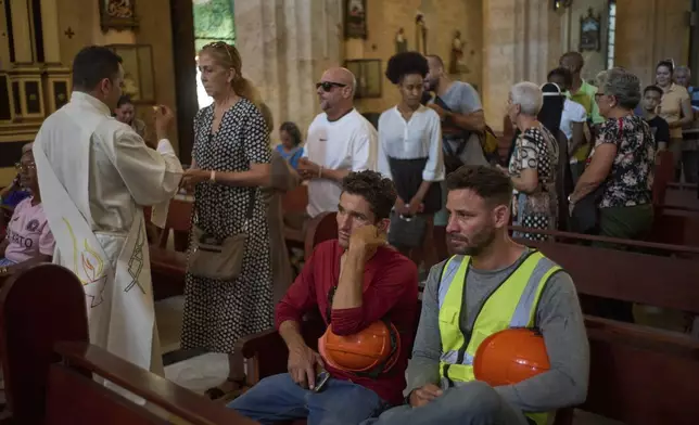 Construction workers Yosbel Castillo, center, and José Sanchez, right, attend a Mass honoring the late Pope Francis at Our Lady of Cobre Church in Havana, Monday, April 21, 2025. (AP Photo/Ramon Espinosa)