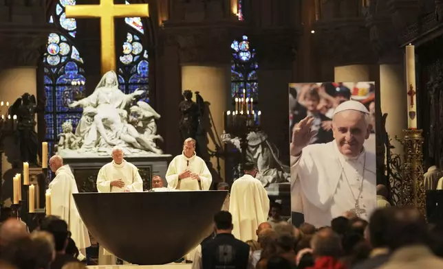 People attend a mass inside Notre Dame cathedral where a poster shows Pope Francis following the Vatican's announcement of his death, Monday, April 21, 2025 in Paris. (AP Photo/Thibault Camus)