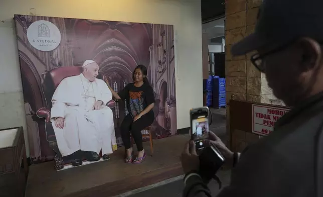 A woman has her photo taken with of a cutout of Pope Francis at the the Cathedral of Our Lady of the Assumption, which was visited by the pope in 2024, in Jakarta, Indonesia, Monday, April 21, 2025. (AP Photo/Achmad Ibrahim)