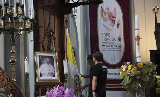 Church officials prepare the portrait of Pope Francis and a Vatican flag ahead of a mass at the the Cathedral of Our Lady of the Assumption, which was visited by Pope Francis in 2024, in Jakarta, Indonesia, Monday, April 21, 2025. (AP Photo/Achmad Ibrahim)