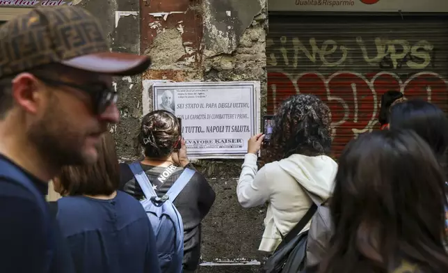 People photograph a mourning poster on the wall in central Naples, southern Italy, reading in Italian: 'You were the Pope of the last, with the ability to fight the first. Thank you for everything... Naples greets you", the day Pope Francis died at the Vatican, Monday, April 21, 2025. (AP Photo/Salvatore Laporta)