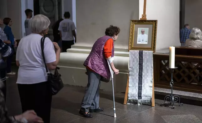 People stand next to a photograph of Pope Francis placed at Cathedral Basilica of Vilnius, Lithuania, Monday, April 21, 2025. (AP Photo/Mindaugas Kulbis)