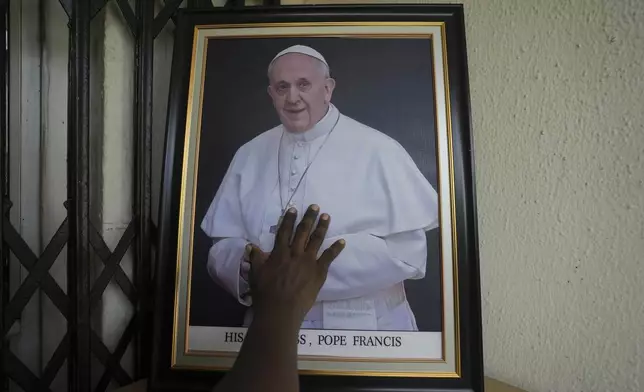A man touches a portrait of the late Pope Francis placed in one of the offices at the Catholic Church of the assumption in Lagos, Nigeria, Monday, April 21, 2025. (AP Photo/Sunday Alamba)