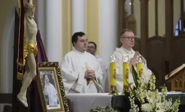 Catholic priests lead a religious service near a photo of the late Pope Francis after the news of his death at age 88 at the Cathedral of the Immaculate Conception in Moscow, Russia, Monday, April 21, 2025. (AP Photo/Pavel Bednyakov)