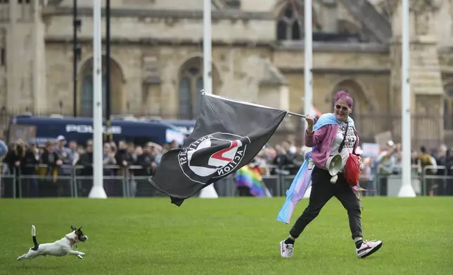 A person with a dog runs across Parliament Square as they take part in a rally organised by trans rights groups, trade unions, and community organisations following the Supreme Court ruling on the definition of a woman in equalities law, at Parliament Square, central London, Saturday April 19, 2025. (AP Photo/Alastair Grant)