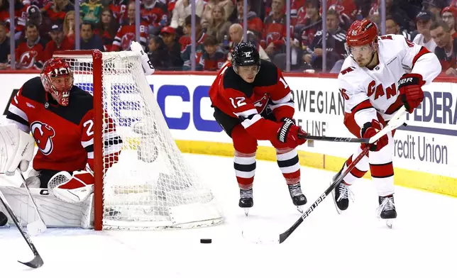 Carolina Hurricanes center Jack Roslovic (96) passes the puck against New Jersey Devils center Cody Glass (12) and goalie Jacob Markstrom (25) during the second period of Game 3 of a first-round NHL hockey playoff series Friday, April 25, 2025, in Newark, N.J. (AP Photo/Noah K. Murray)