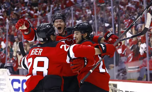 New Jersey Devils Nico Hischier , right, celebrates with Ondrej Palat and Timo Meier (28) after scoring against the Carolina Hurricanes during the first period of Game 3 of a first-round NHL hockey playoff series Friday, April 25, 2025, in Newark, N.J. (AP Photo/Noah K. Murray)