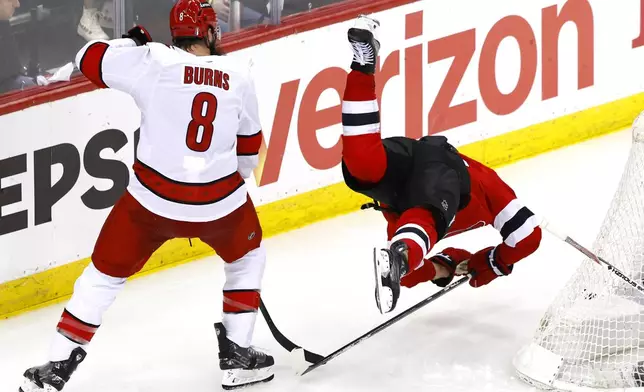 Carolina Hurricanes defenseman Brent Burns (8) trips New Jersey Devils right wing Timo Meier, right, during overtime of Game 3 in a first-round NHL hockey playoff series Friday, April 25, 2025, in Newark, N.J. (AP Photo/Noah K. Murray)