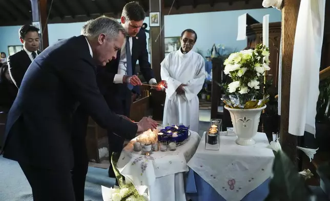 Liberal Leader Mark Carney, British Columbia Premier David Eby and Vancouver Mayor Ken Sim light candles as they visit St. Mary the Vigil South Hill Church as Fr. Expedito Farinas looks on, after a vehicle drove into a crowd during a Filipino heritage festival in Vancouver, British Columbia, Sunday, April 27, 2025. (Sean Kilpatrick/The Canadian Press via AP)