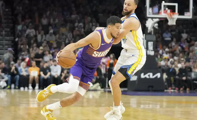 Phoenix Suns guard Devin Booker (1) works to get around Golden State Warriors guard Stephen Curry, right, during the first half of an NBA basketball game in Phoenix, Tuesday, April 8, 2025. (AP Photo/Darryl Webb)