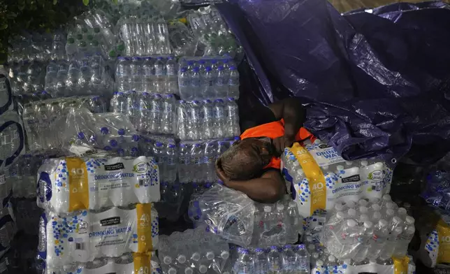 A man sleeps on bottles of water in Santo Domingo, Dominican Republic, Thursday, April 10, 2025, in front of the Jet Set nightclub after its roof collapsed during a merengue concert. (AP Photo/Matias Delacroix)