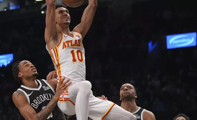 Atlanta Hawks' Zaccharie Risacher (10) dunks the ball in front of Brooklyn Nets' Nic Claxton (33) and Tosan Evbuomwan (12) during the first half of an NBA basketball game Thursday, April 10, 2025, in New York. (AP Photo/Frank Franklin II)