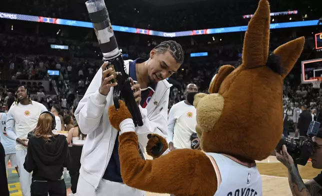 The San Antonio Spurs Coyote, right, teaches Spurs forward Victor Wembanyama how to use the tee shirt cannon after an NBA basketball game against the Toronto Raptors, Sunday, April 13, 2025, in San Antonio. (AP Photo/Darren Abate)