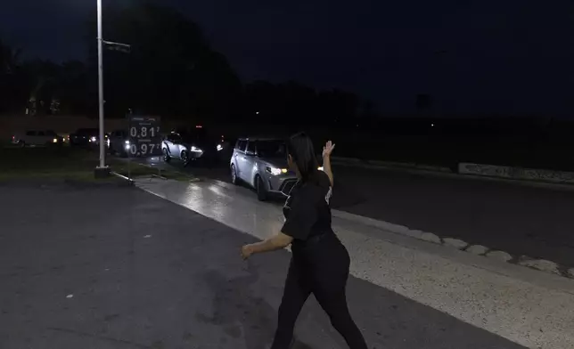 A gas station employee directs traffic as cars line up for fuel during an island-wide blackout in San Juan, Puerto Rico, Wednesday, April 16, 2025. (AP Photo/Alejandro Granadillo)