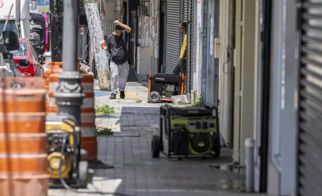 Generators line the sidewalk of a commercial street in Barrio Obrero as shops try to remain open during a prolonged power outage in San Juan, Puerto Rico, Thursday, April 17, 2025. (AP Photo/Alejandro Granadillo)