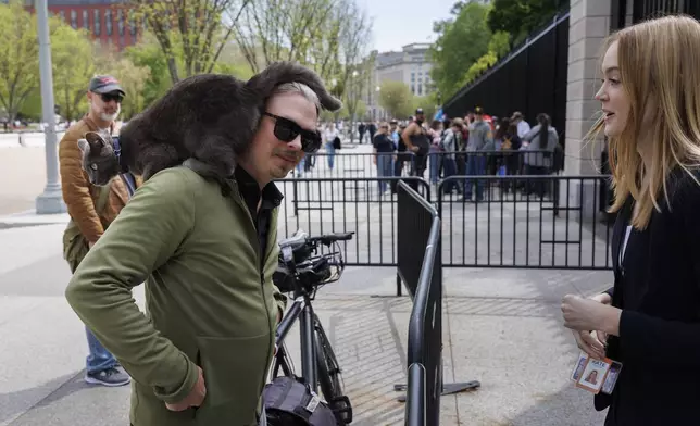 Reporter Kate Sullivan, right, delivers Sophie, a cat found wandering the White House Grounds, to its owner Alec Augustine outside the White House, Friday, April 18, 2025, in Washington. (AP Photo/Tom Brenner)