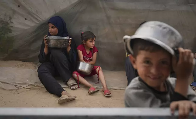 Mira Abu Shaar, 5, right, and her older sister, Raghad, 15, hold pots next to their family tent, as they wait for food to be prepared, in Muwasi, on the outskirts of Khan Younis in the southern Gaza Strip, Thursday, April 24, 2025. (AP Photo/Abdel Kareem Hana)