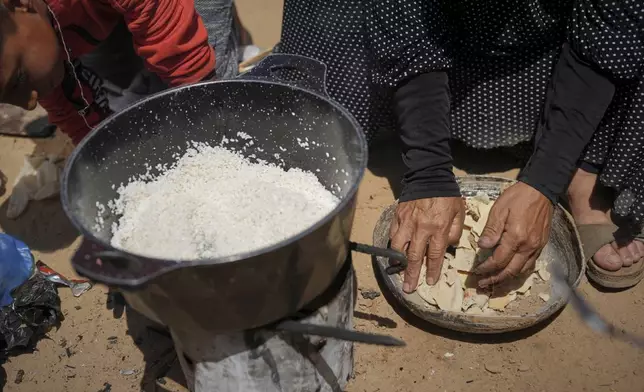 Sumaya Al-Najjar, 60, cuts stale bread to mix with rice to cook over a fire next to her family tent in Muwasi, on the outskirts of Khan Younis in the southern Gaza Strip, Friday, April 25, 2025. (AP Photo/Abdel Kareem Hana)