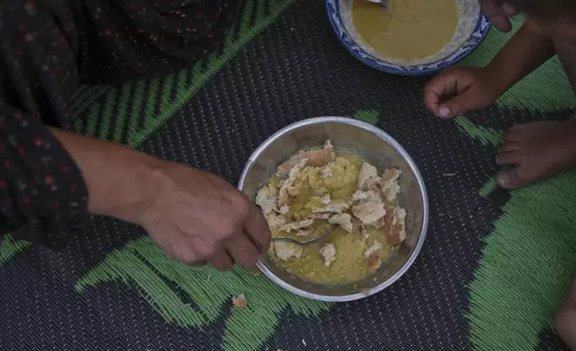Abeer Abu Shaar, 45, prepares a dish of bread mixed with lentil soup for her son, Ibrahim, 3, in their tent at Muwasi, on the outskirts of Khan Younis, in the southern Gaza Strip, Thursday, April 24, 2025. (AP Photo/Abdel Kareem Hana)