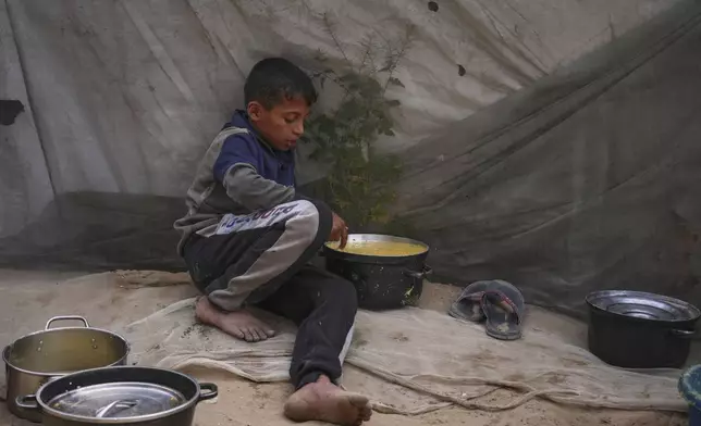 Mohammad Abu Zeid, 12, tastes the food prepared for a meal in his family tent in Muwasi, on the outskirts of Khan Younis in the southern Gaza Strip, Thursday, April 24, 2025. (AP Photo/Abdel Kareem Hana)