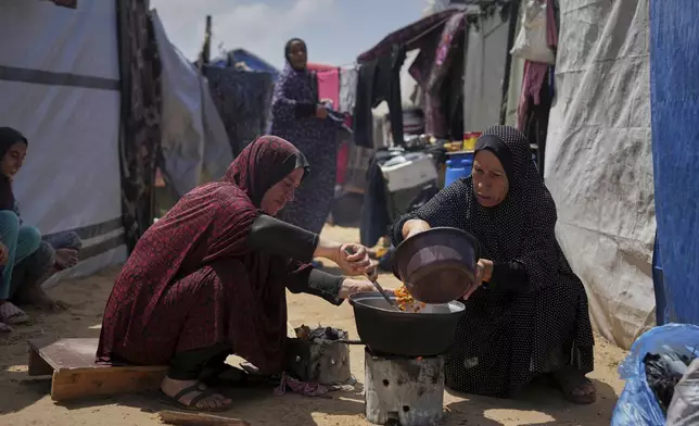 Sumaya Al-Najjar, 60, left, and Etemad Al-Maghari, 52, pour peas into a pot to cook over a fire next to their tents in Muwasi, on the outskirts of Khan Younis in the southern Gaza Strip, Friday, April 25, 2025. (AP Photo/Abdel Kareem Hana)