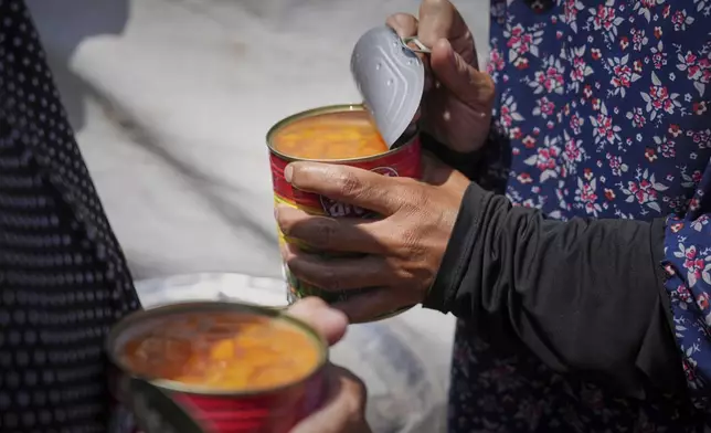 Maryam Al-Najjar, 38, opens a can of peas to prepare them for cooking in her family's tent in Muwasi, on the outskirts of Khan Younis in the southern Gaza Strip, Friday, April, 25, 2025. (AP Photo/Abdel Kareem Hana)