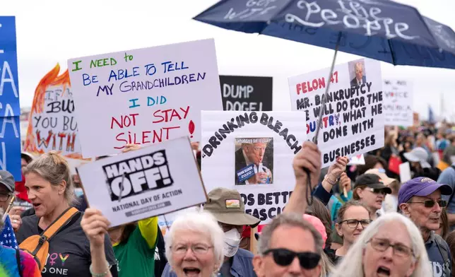 Demonstrators hold up signs during a "Hands Off!" protest against President Donald Trump at the Washington Monument in Washington, Saturday, April 5, 2025. (AP Photo/Jose Luis Magana)