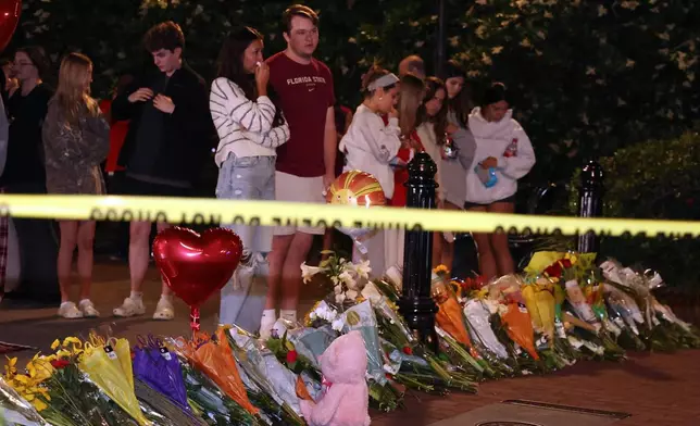 An impromptu memorial shared online brings students bearing flowers into the evening near the center of the Florida State campus in sight of the Student Union building, Tallahassee, Fla., Thursday, April 17, 2025. (AP Photo/Gary McCullough)