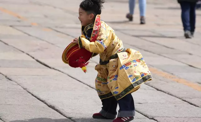 A child dressed as the emperor reacts after retrieving his crown blown away outside the Forbidden City during high winds in Beijing, China, Saturday, April 12, 2025. (AP Photo/Ng Han Guan)