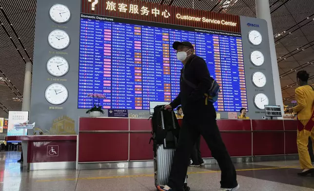 A traveller walks past by a board showing flights that are cancelled at the Capital International Airport Terminal 3 following gale wind alerts in Beijing, China, Saturday, April 12, 2025. (AP Photo/Ng Han Guan)
