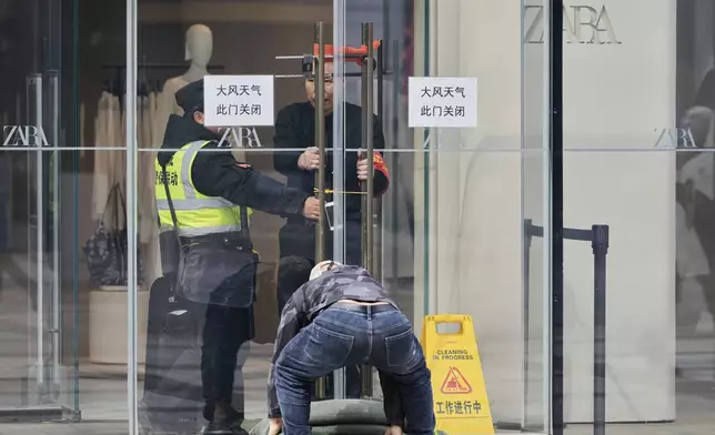 Security personnel secure a glass door with locks and sandbags near signs which reads "Windy Weather, This Door Shut" at the Wangfujing Shopping Street in Beijing, China, Saturday, April 12, 2025. (AP Photo/Ng Han Guan)