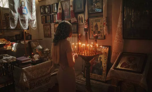 A woman lights a candle during the celebration of Orthodox Easter at St. John Theologian Church of the Orthodox Church of Ukraine in Kharkiv, Ukraine, on Sunday, April 20, 2025. (AP Photo/George Ivanchenko)