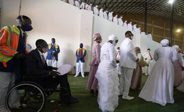 A groom in a wheelchair is assisted by a fellow member whilst his two brides walk in front, during mass Easter weddings for 3,000 people, some polygamous, at The International Pentecost Holiness Church in Heidelberg, east of Johannesburg, South Africa, Sunday, April 20, 2025. (AP Photo/Themba Hadebe)