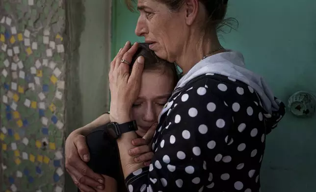 A mother calms her daughter during farewell ceremony of Maksym Martynenko, 11, Natalia Martynenko, 49, Mykola Martynenko, 41, which were killed in a deadly Palm Sunday Russian attack on Sumy on April 13, during farewell ceremony in Stare Selo village near Sumy, Ukraine, April 16, 2025. (AP Photo/Evgeniy Maloletka)