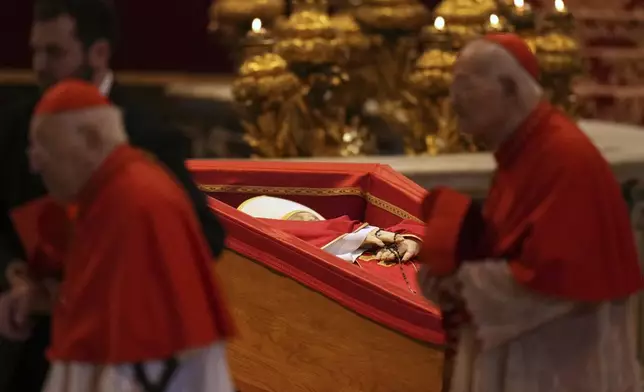 Cardinals walk past the body of Pope Francis, who will lie in state for three days, after it arrived in St. Peter's Basilica at the Vatican, Wednesday, April 23, 2025. (AP Photo/Francisco Seco)