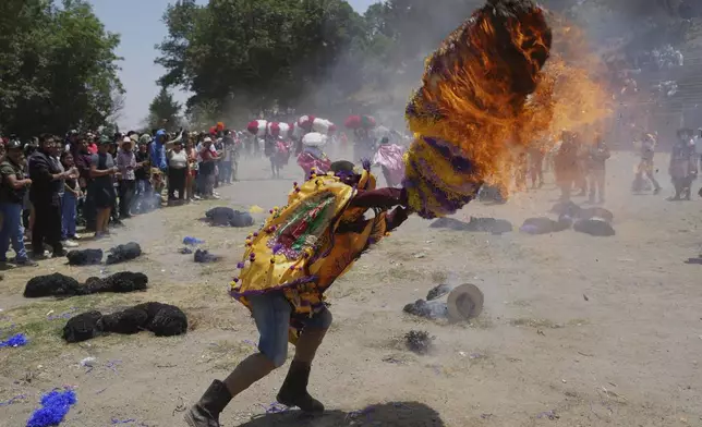 A reveler, known as a sayon, tries to put out a fire he started on a tissue paper hat as part of Easter celebrations in Tetela del Volcan, Mexico, Sunday, April 20, 2025. (AP Photo/Eduardo Verdugo)